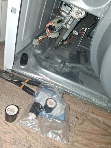 Gas dryer with the front panel removed and replacement gas valve coils ready to install